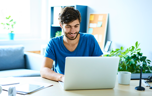 Young man working on laptop in home office and smiling